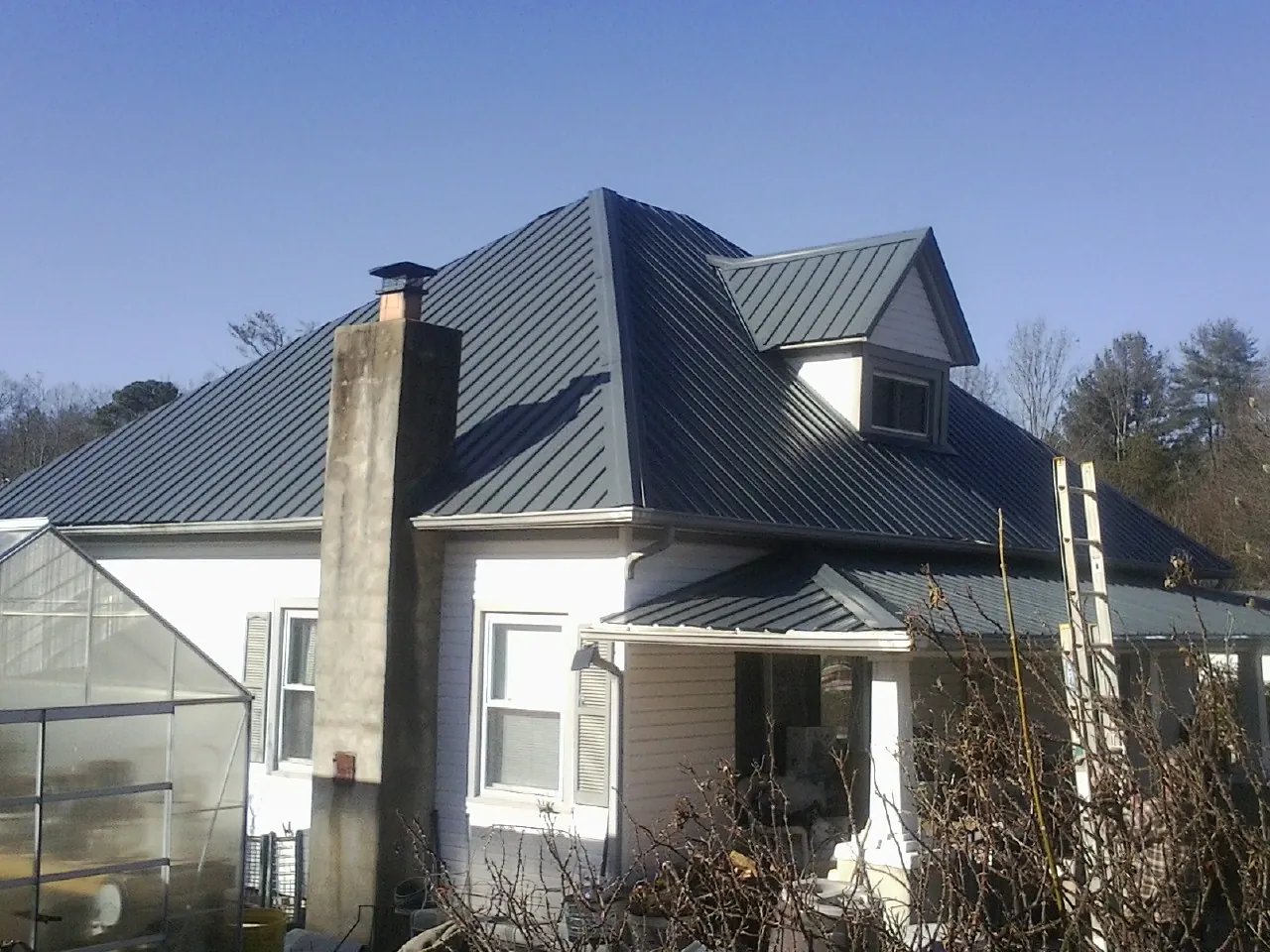 Dark blue standing seam metal roof on a white farmhouse with dormer — Slate & Tile Roof Repair by Roofing Brothers in Nellis Afb