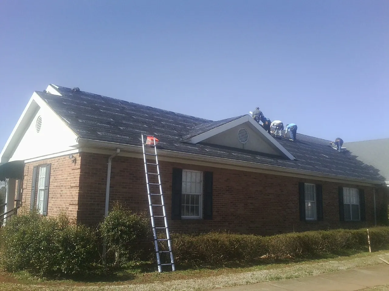 Crew tearing shingles off a brick ranch roof with a ladder set — Emergency Roof Repair work by our crew in Nellis Afb
