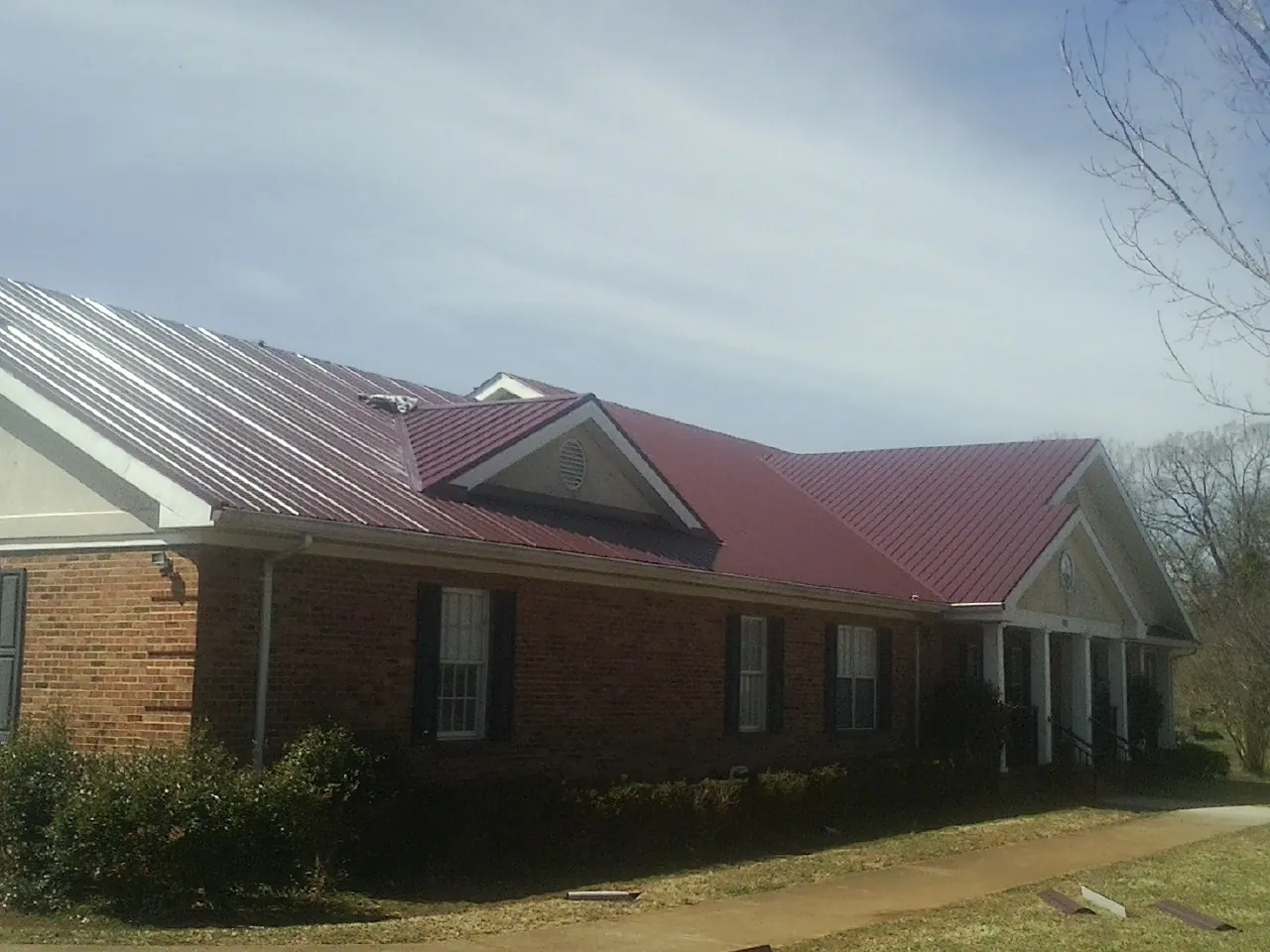 Red metal roof with gabled entries on a long brick building, from a Hail Damage Roof Repair job in Nellis Afb