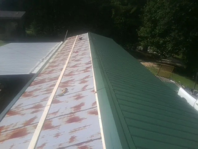 Old rusted panels beside newly installed green metal roofing — Wind Damage Roof Repair by Roofing Brothers in Nellis Afb