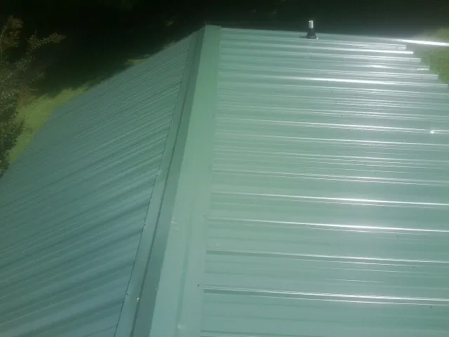 New green metal panels meeting at the ridge of a roof — Flat Roof Repair work by our crew in Nellis Afb