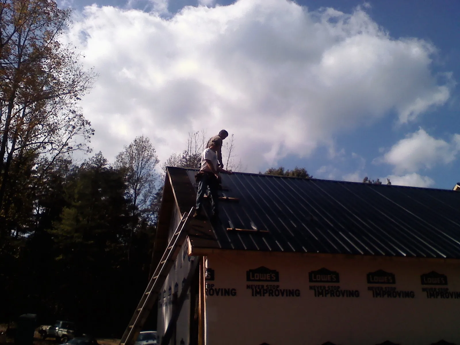 Roofer fastening dark metal panels high against a cloudy sky, from a Roof Inspection job in Nellis Afb