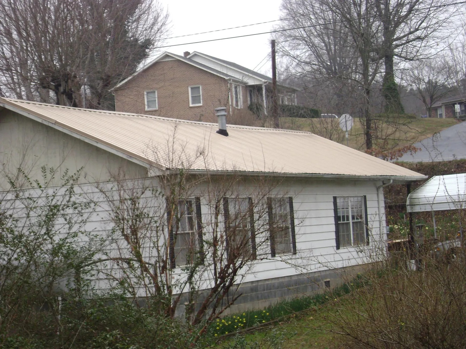 Tan metal roof on a white sided house set into a hillside — Commercial Roofing by Roofing Brothers in Nellis Afb